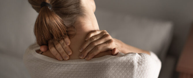woman is holding neck with both hands as if in pain