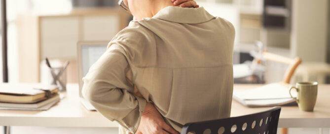 Woman at her desk holding her neck and lower back in discomfort, representing Rolfing® for desk workers in Rockville, MD